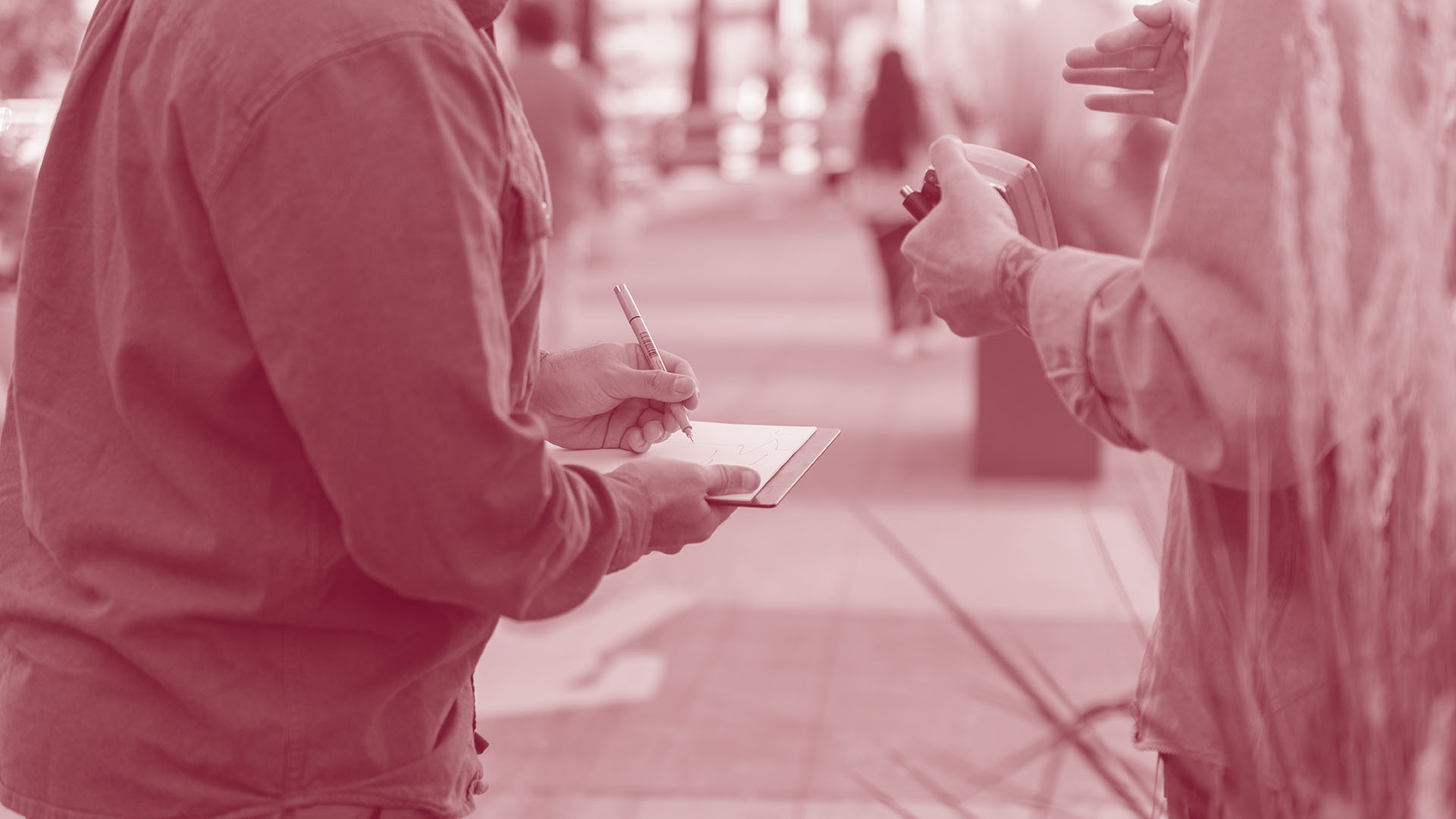 Two students standing along a pedestrian pathway with one student writing in a notebook.