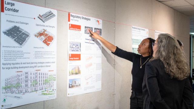 A student points to her poster about regulatory strategies for a large corridor as she presents her work to a reviewer in the 3rd Floor Octagon in the College of Architecture and Planning.