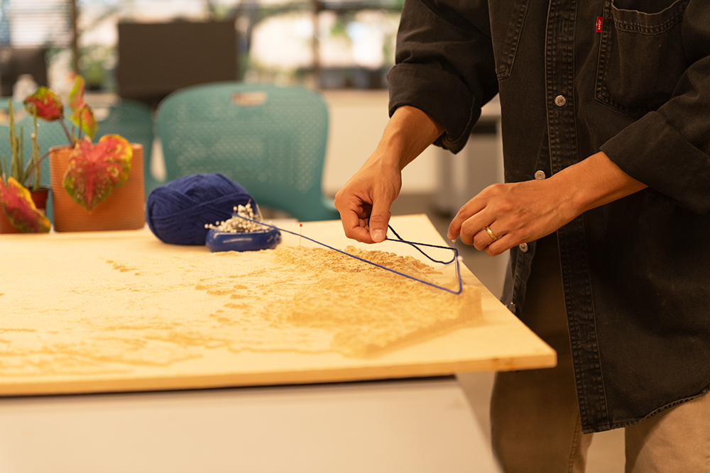 A person's hands are working with yarn to on a topographical model.
