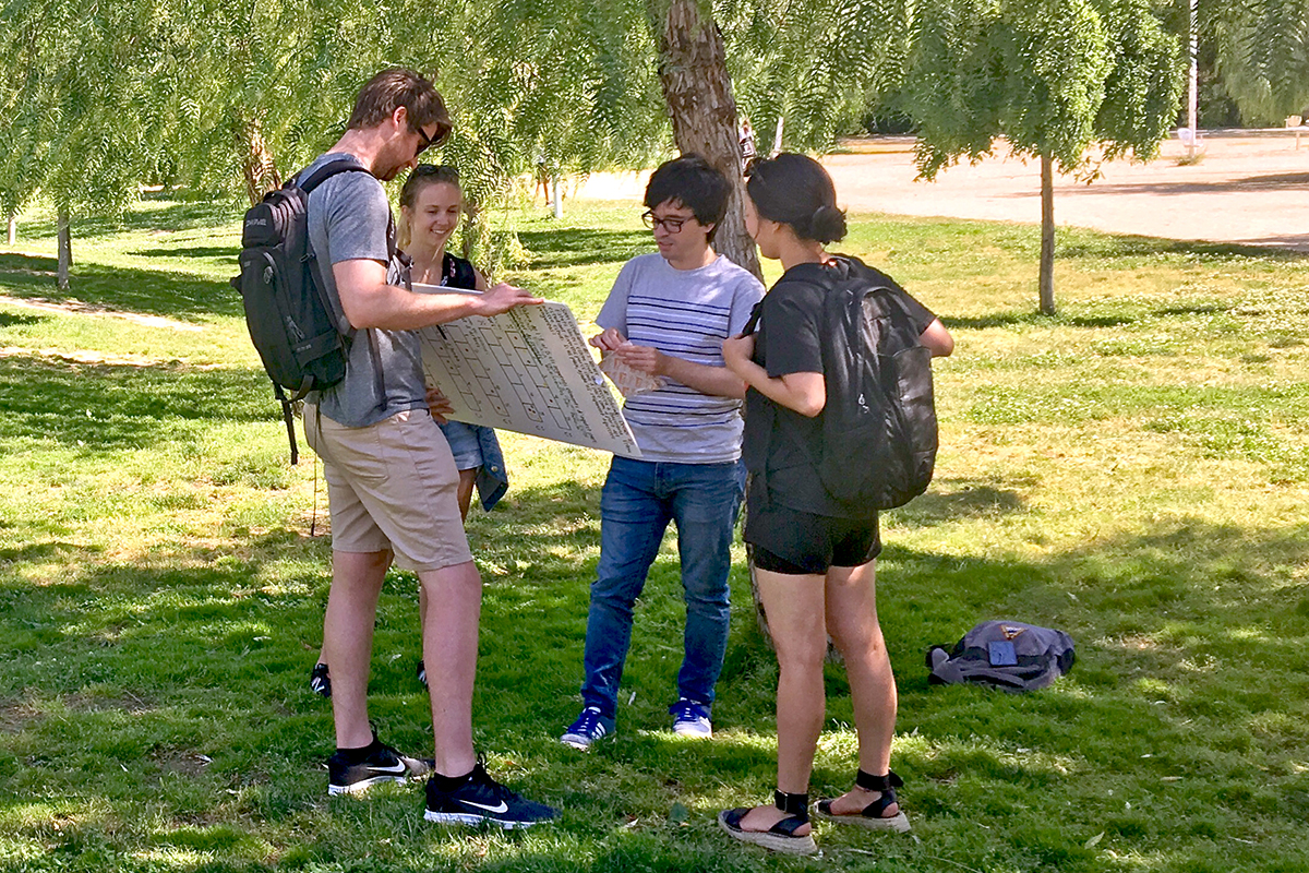 Four MUD students standing outside in a circle looking at a poster.