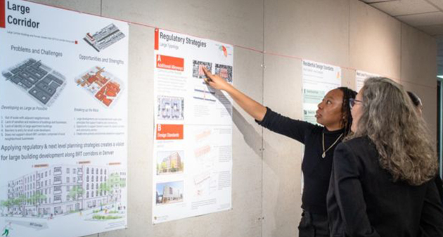 A student speaks with a reviewer in the College of Architecture and Planning's 3rd floor octagon and points to a poster feaaturing regulatory strategies for a large corridor.