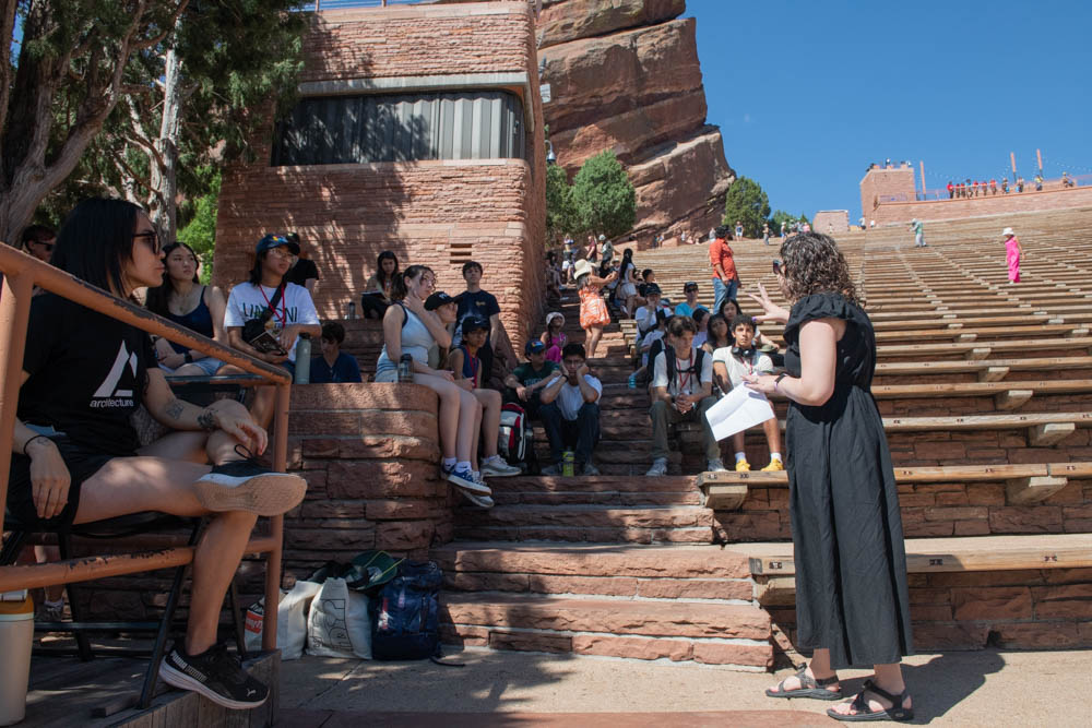 Students sitting on the steps at Red Rocks listening to a presentation about the space on a sunny day.