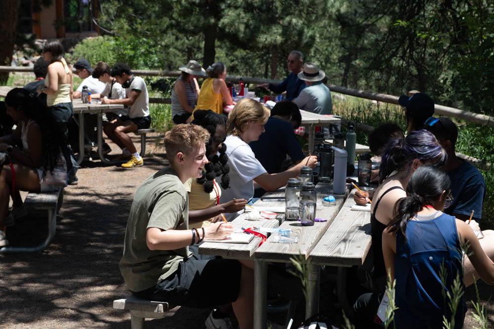 A large group of students sitting outside sketching at a park on a sunny day.