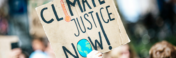 A hand holding up a cardboard sign that says Environmental Justice Now.