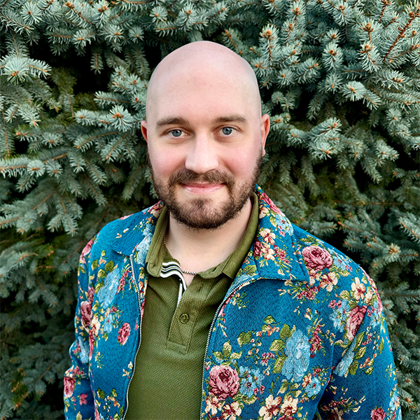 Connor Rumsey standing in front of an evergreen tree wearing a floral jacket.