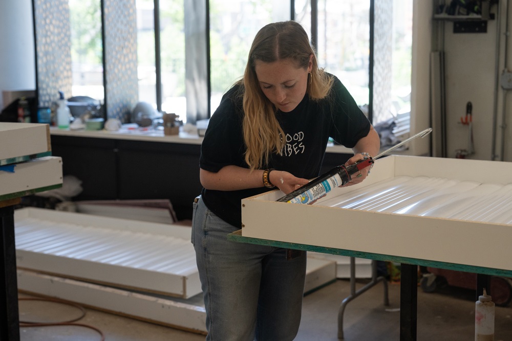 A student caulking interior walls of the kiosk.