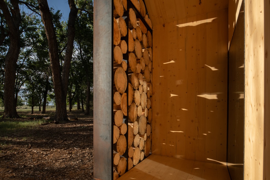 A view of the interior of the Aiken Audubon Research Outpost focused on the shadows cast through the logs on the facade.