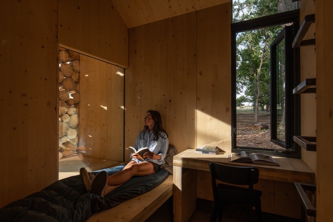 A student sitting on a sleeping bag while reading a book in the cabin's dorm