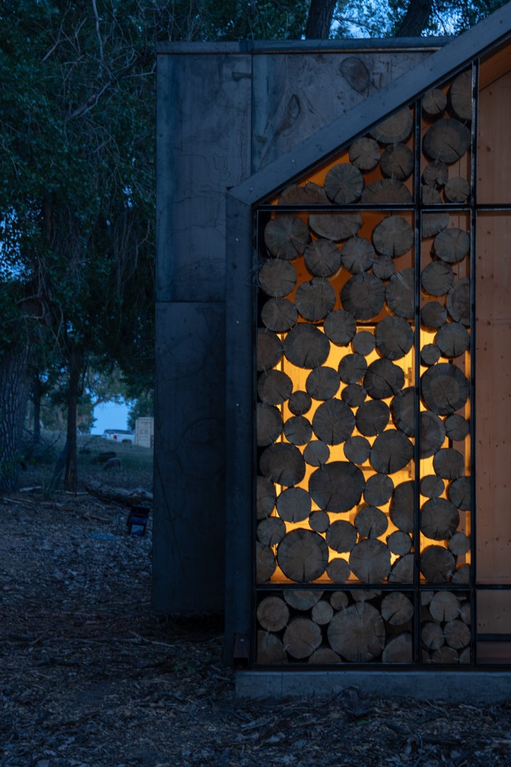 The  Aiken Audubon Research Outpost at night, showing the light shining through the logs on the exterior facade.